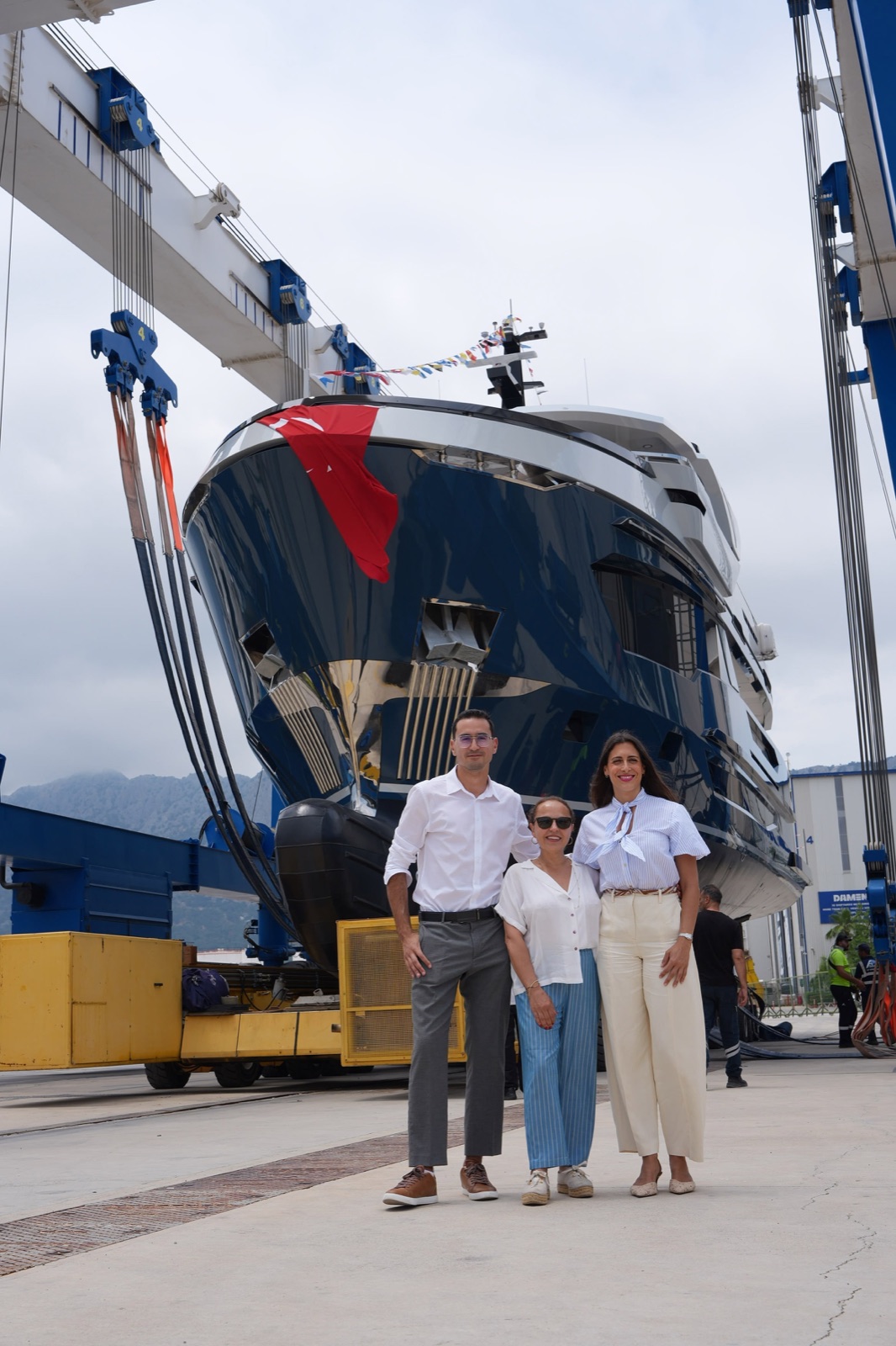 The AvA Yachts Kando 85 in the travel lift on launch day, dressed with signal flags, with three of the team standing under her bow