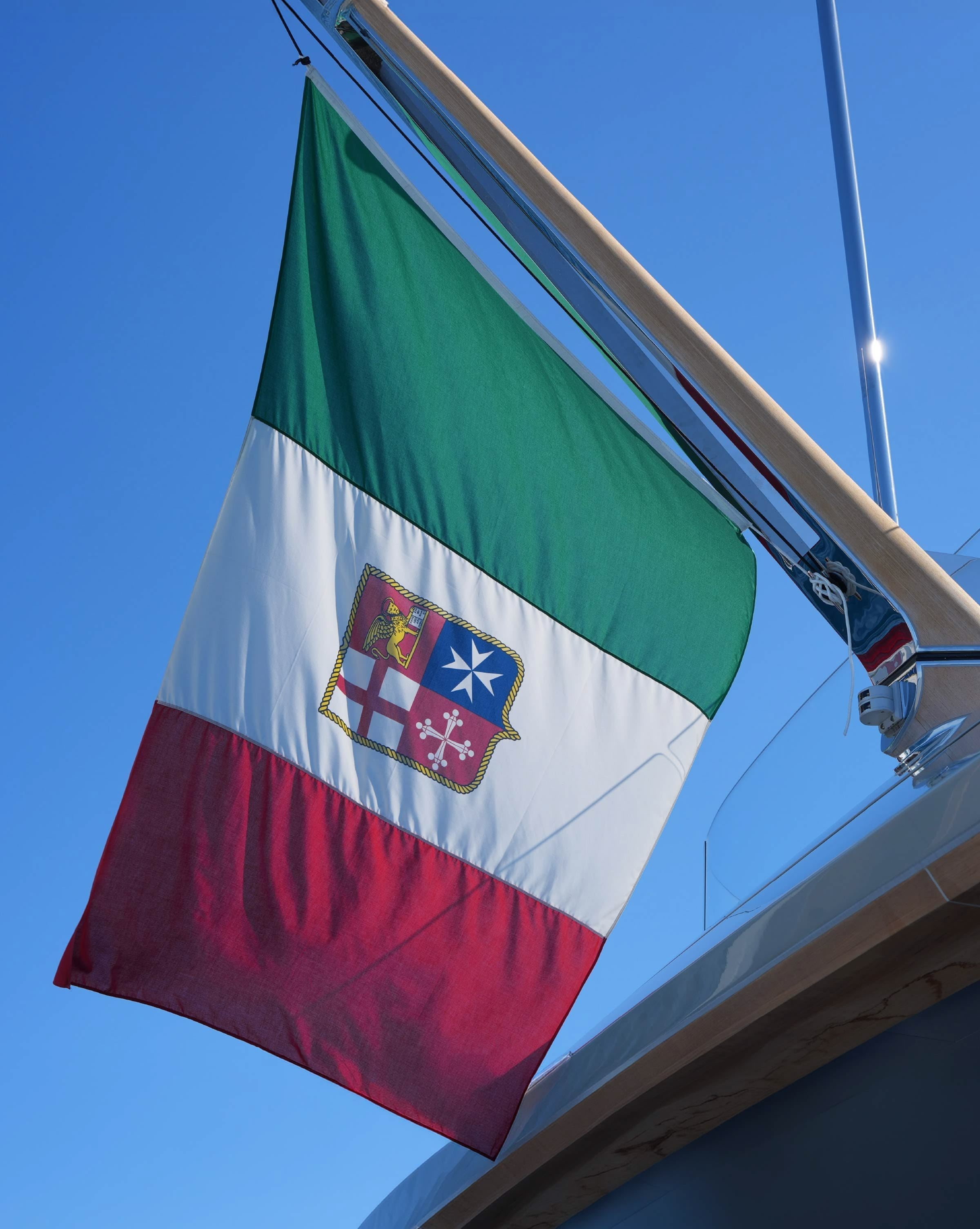 The Italian ensign flying from a yacht backstay against a clear blue sky.