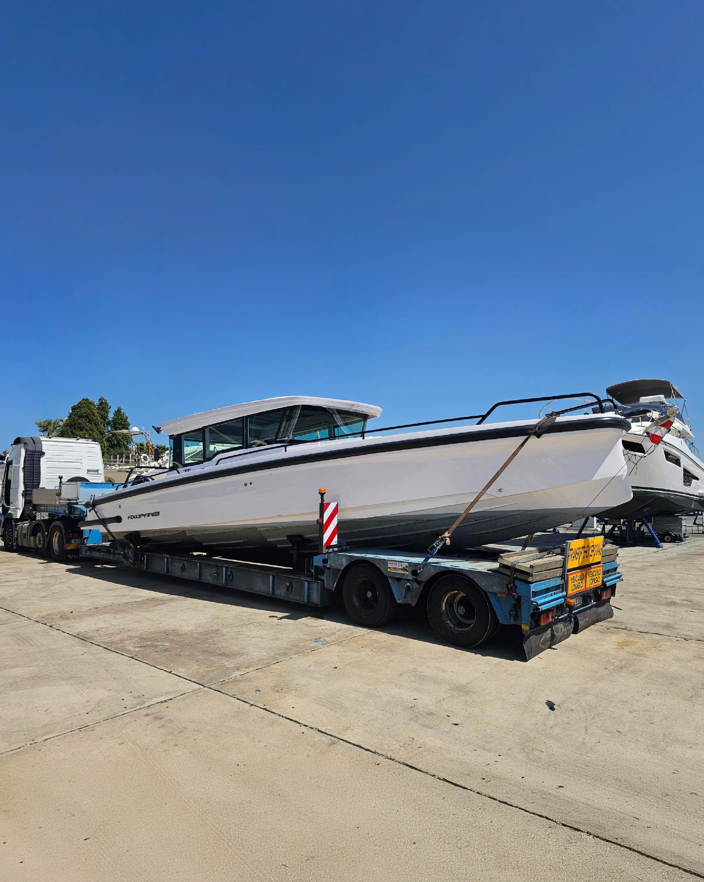 A motor yacht strapped down on a low loader trailer on a hard standing, ready to travel by road.